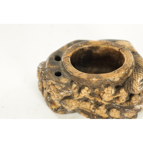 236 - A CARVED CHINESE SOAPSTONE BRUSH POT carved with figures on a rocky outcrop. (9.5cm wide)