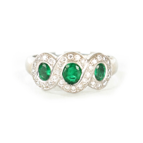 310 - A LADIES 18CT WHITE GOLD THREE STONE EMERALD AND DIAMOND RINGE with a continuous triple loop diamond... 