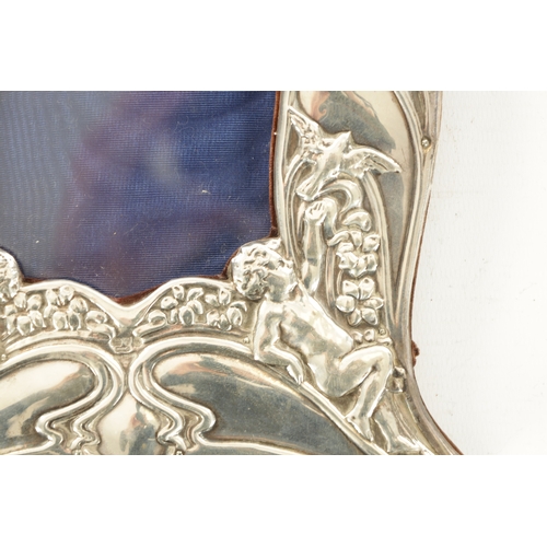 441 - AN ART NOUVEAU SILVER FRAME with shaped border depicting winged cherubs amongst leafing branchwork a... 