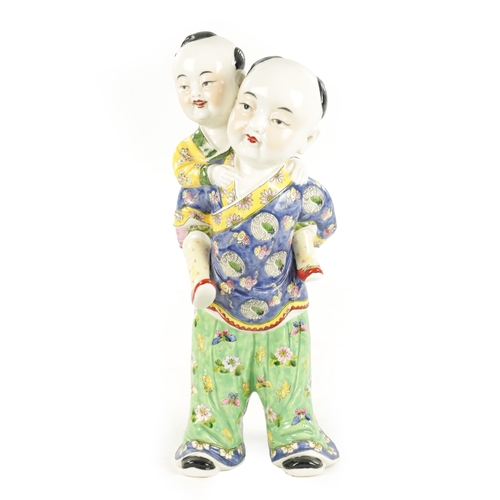 94 - A LATE 19TH CENTURY CHINESE PORCELAIN FIGURE modelled as a boy giving a piggyback dressed in brightl... 