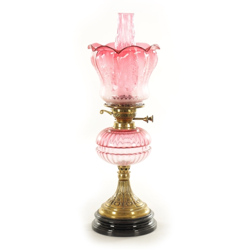 685 - A GOOD VICTORIAN CRANBERRY GLASS AND BRASS OIL LAMP with black pottery foot and stylised leaf work b... 