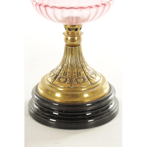 685 - A GOOD VICTORIAN CRANBERRY GLASS AND BRASS OIL LAMP with black pottery foot and stylised leaf work b... 