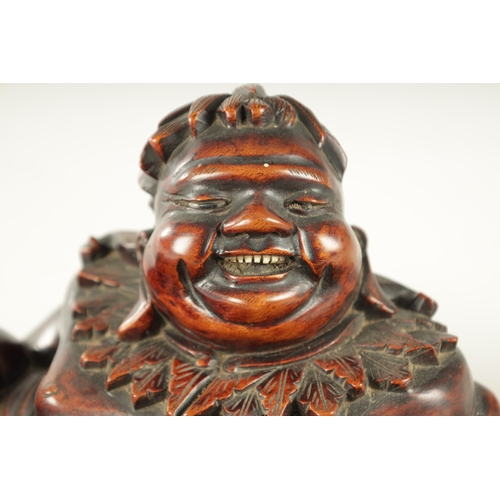 128 - A LATE 19TH CENTURY CHINESE CARVED HARDWOOD SCULPTURE modelled as Hotei in a reclining pose beside a... 