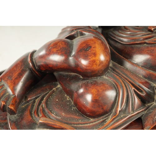 128 - A LATE 19TH CENTURY CHINESE CARVED HARDWOOD SCULPTURE modelled as Hotei in a reclining pose beside a... 