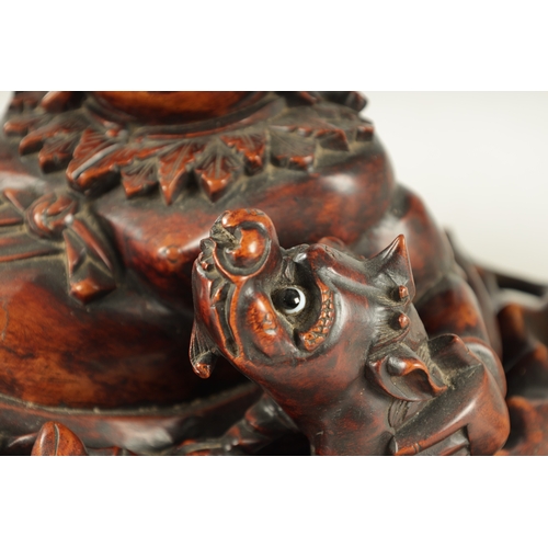 128 - A LATE 19TH CENTURY CHINESE CARVED HARDWOOD SCULPTURE modelled as Hotei in a reclining pose beside a... 