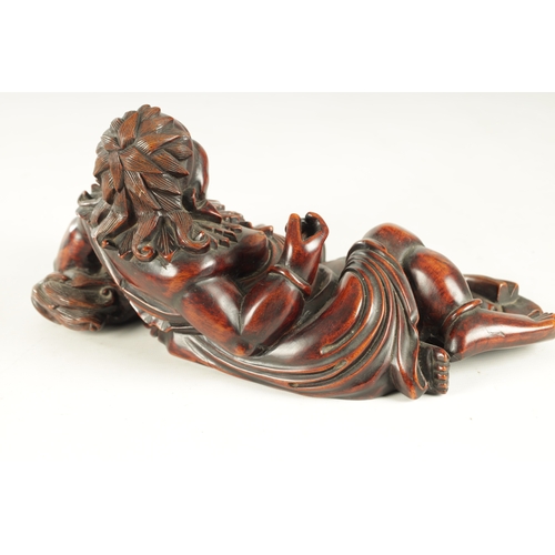 128 - A LATE 19TH CENTURY CHINESE CARVED HARDWOOD SCULPTURE modelled as Hotei in a reclining pose beside a... 