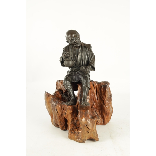 215 - A LARGE JAPANESE MEIJI PERIOD OKIMONO ON ROOT WOOD BASE depicting a robed elder seated with a teapot... 