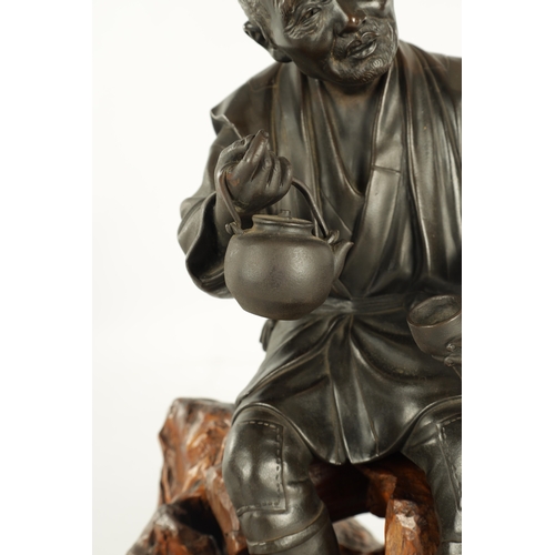 215 - A LARGE JAPANESE MEIJI PERIOD OKIMONO ON ROOT WOOD BASE depicting a robed elder seated with a teapot... 