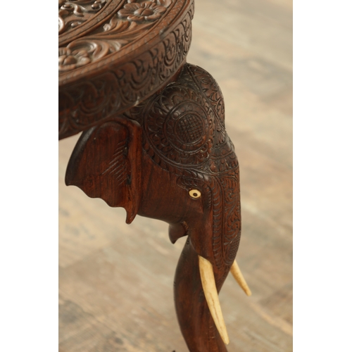 245 - A 19TH CENTURY INDIAN CARVED HARDWOOD OCCASIONAL TABLE the circular carved top above three elephant'... 