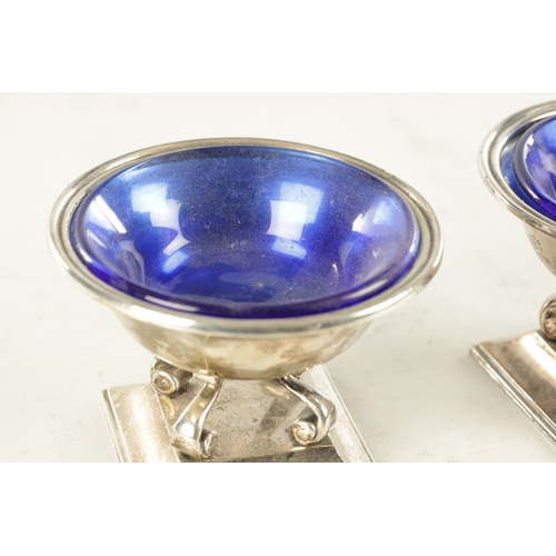 443 - A PAIR OF SILVER SALT CELLARS WITH BLUE GLASS LINERS, raised on scrolled supports and square moulded... 