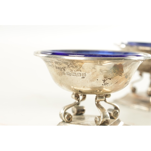 443 - A PAIR OF SILVER SALT CELLARS WITH BLUE GLASS LINERS, raised on scrolled supports and square moulded... 