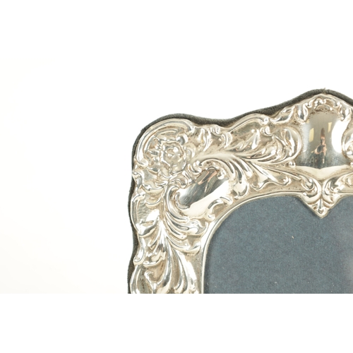 487 - A VICTORIAN STYLE SILVER PHOTOGRAPH FRAME with embossed scrolling leafwork surround and arched top c... 