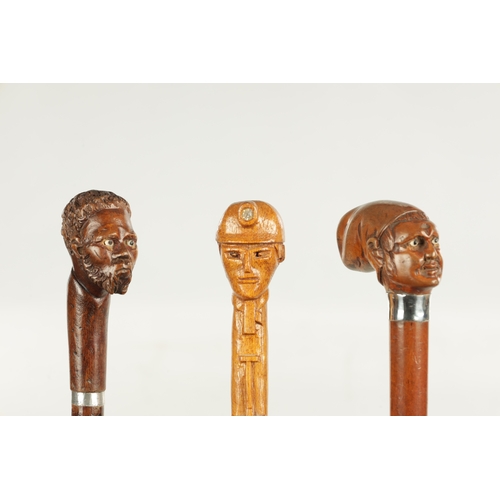 496 - A COLLECTION OF THREE LATE 19TH CENTURY CARVED WOOD MASK HEAD WALKING STICKS one with silver collar ... 