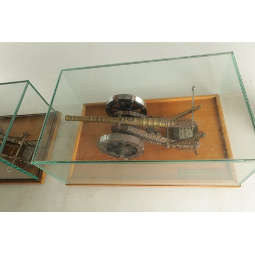 650 - TWO 20TH CENTURY BRONZE MODEL CANNON on wooden carriages - in glass display cabinets (32cm wide )