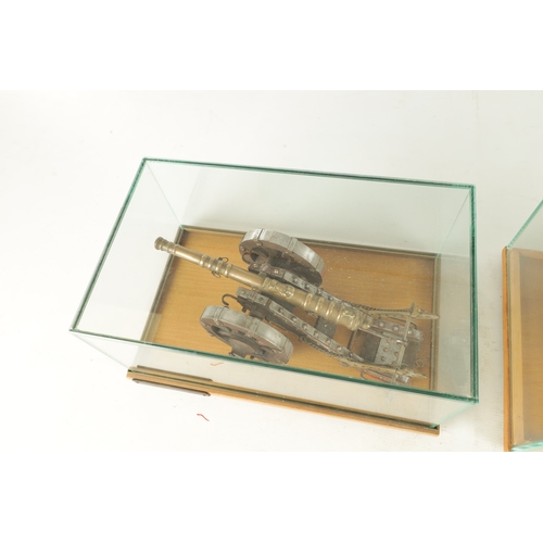 650 - TWO 20TH CENTURY BRONZE MODEL CANNON on wooden carriages - in glass display cabinets (32cm wide )