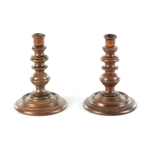 913 - A PAIR OF 19TH CENTURY TURNED WALNUT TREENWARE CANDLESTICKS having knopped turned stems and dished b... 