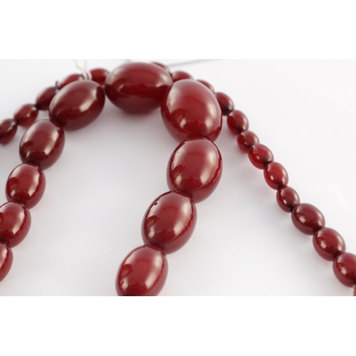 102 - A GRADUATED CHERRY AMBER OVAL BEAD NECKLACE, with red string, largest bead measures 28mm long. Total... 