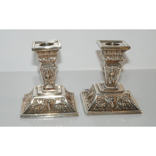 811 - A pair of silver dwarf candlesticks with fixed sconces on square tapering stems with foliate embosse... 