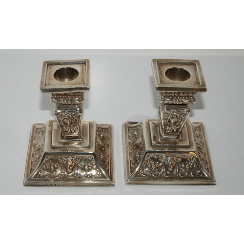 811 - A pair of silver dwarf candlesticks with fixed sconces on square tapering stems with foliate embosse... 