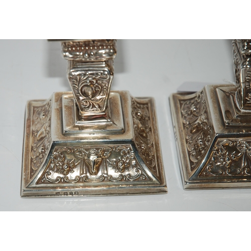 811 - A pair of silver dwarf candlesticks with fixed sconces on square tapering stems with foliate embosse... 