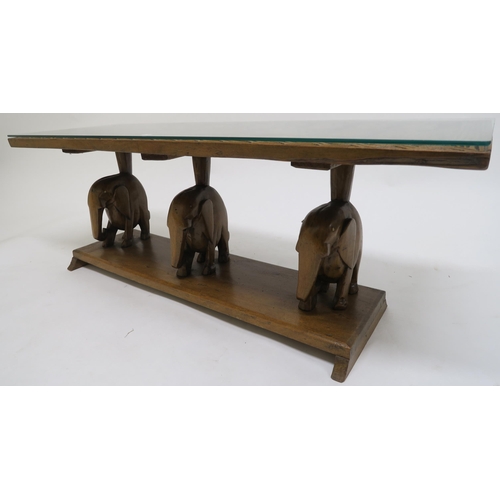 77 - A 20th century carved African hardwood coffee table with carved elephant supports, 43cm high x 122cm... 