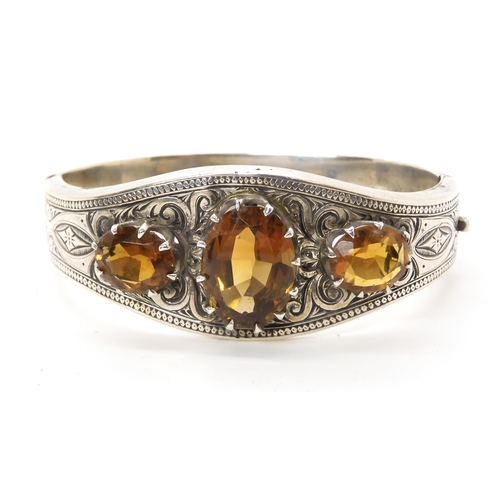 664 - A white metal bangle set with citrines, with hand engraved decoration