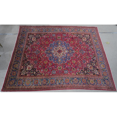 121 - A RED GROUND PERSIAN HAND KNOTTED MASHAD RUG with cream and blue central medallion,matching blue bor... 