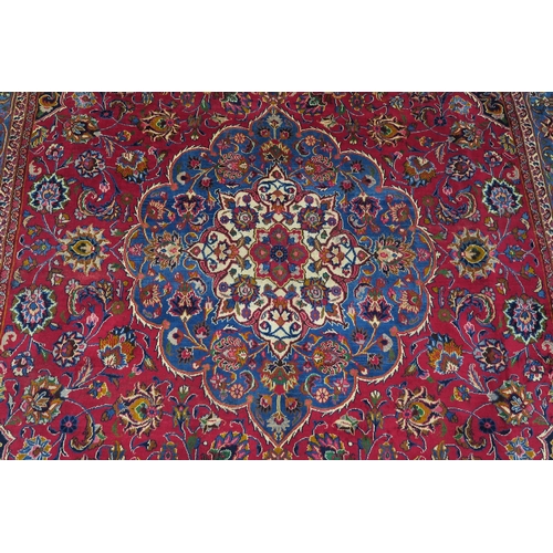 121 - A RED GROUND PERSIAN HAND KNOTTED MASHAD RUG with cream and blue central medallion,matching blue bor... 