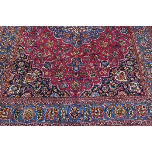 121 - A RED GROUND PERSIAN HAND KNOTTED MASHAD RUG with cream and blue central medallion,matching blue bor... 