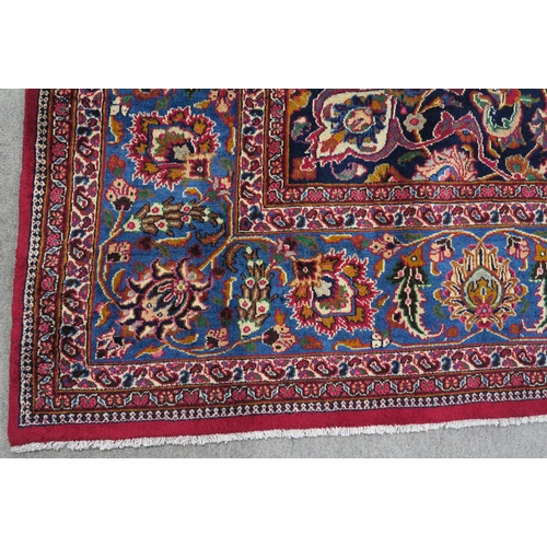 121 - A RED GROUND PERSIAN HAND KNOTTED MASHAD RUG with cream and blue central medallion,matching blue bor... 