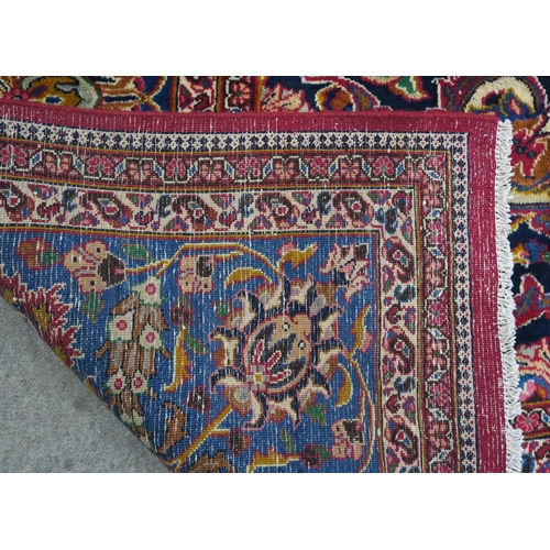 121 - A RED GROUND PERSIAN HAND KNOTTED MASHAD RUG with cream and blue central medallion,matching blue bor... 