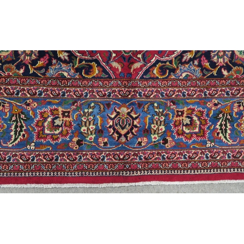 121 - A RED GROUND PERSIAN HAND KNOTTED MASHAD RUG with cream and blue central medallion,matching blue bor... 