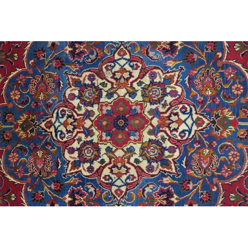 121 - A RED GROUND PERSIAN HAND KNOTTED MASHAD RUG with cream and blue central medallion,matching blue bor... 