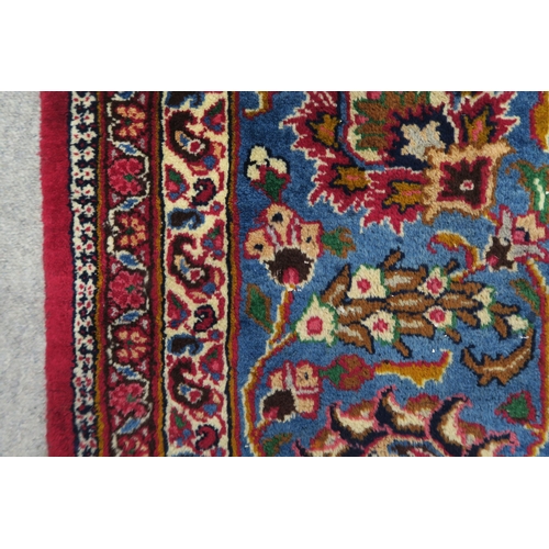 121 - A RED GROUND PERSIAN HAND KNOTTED MASHAD RUG with cream and blue central medallion,matching blue bor... 