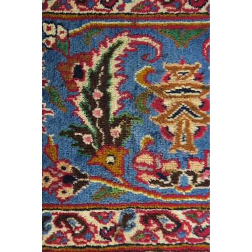 121 - A RED GROUND PERSIAN HAND KNOTTED MASHAD RUG with cream and blue central medallion,matching blue bor... 