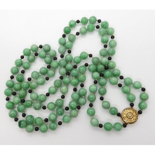 708 - A DOUBLE STRING OF CHINESE GREEN HARDSTONE BEADS WITH A DECORATIVE CLASP the hardstone beads are int... 