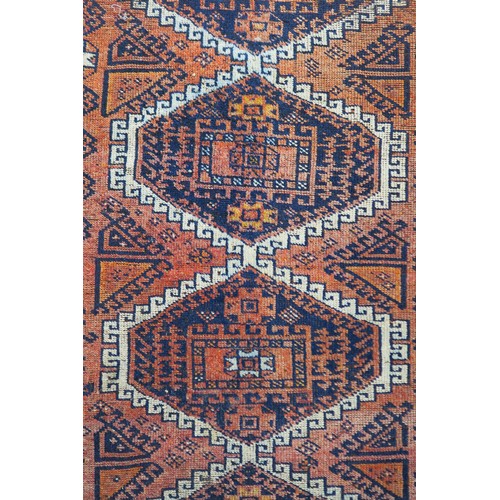 121A - A TERRACOTTA GROUND BELOUCH RUG, with seven geometric medallions and orange border, 310cm long x 138... 