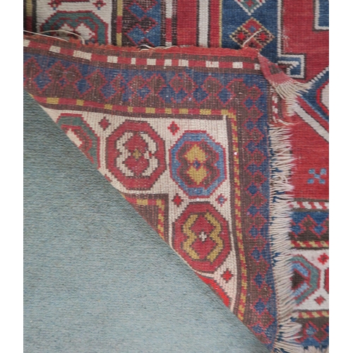 62 - A terracotta ground Caucasian rug with three geometric medallions and multicoloured borders, 240cm l... 