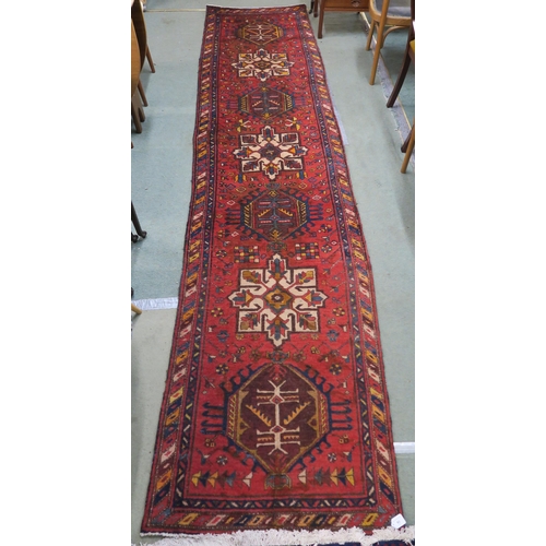 92 - A red ground Heriz runner with geometric medallions and multicoloured border, 381cm long x 88cm wide