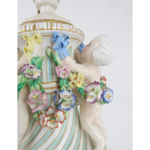 193 - A CONTINENTAL PORCELAIN URN SHAPED LAMPdecorated with putti with swags of flowers and applied roses,... 