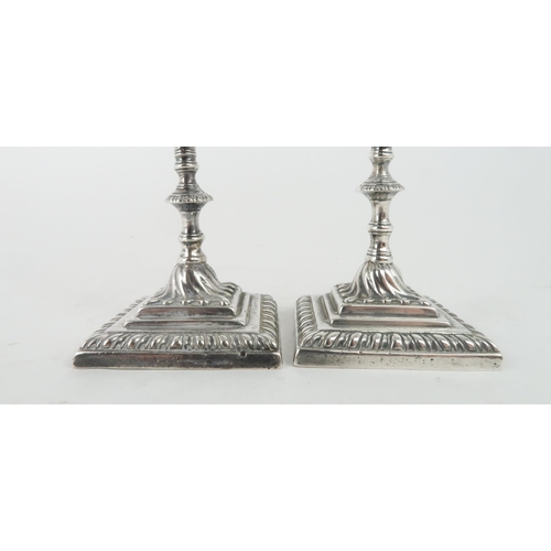 465 - A NEAR PAIR OF GEORGE III CAST SILVER CANDLESTICKSon square footed and gadrooned bases, with swirl c... 