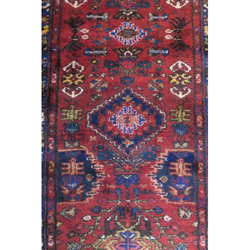 100 - A red ground Iranian Hamedan runner with dark blue borders, 175cm long x 101cm wide