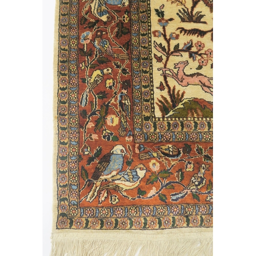 102 - AN EASTERN SILK CREAM GROUND RUG DEPICTING A HUNTING SCENE