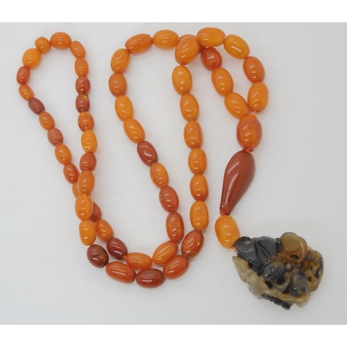 560 - A STRING OF AMBER BEADS WITH A CHINESE CARVED PENDANT