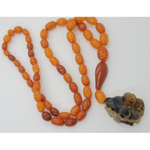 560 - A STRING OF AMBER BEADS WITH A CHINESE CARVED PENDANT