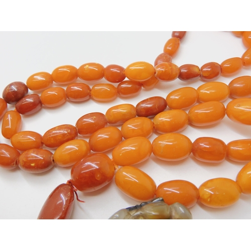 560 - A STRING OF AMBER BEADS WITH A CHINESE CARVED PENDANT