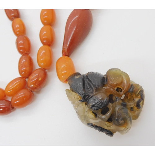 560 - A STRING OF AMBER BEADS WITH A CHINESE CARVED PENDANT