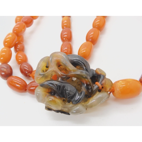 560 - A STRING OF AMBER BEADS WITH A CHINESE CARVED PENDANT