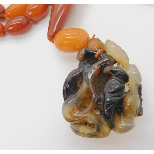 560 - A STRING OF AMBER BEADS WITH A CHINESE CARVED PENDANT