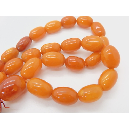 560 - A STRING OF AMBER BEADS WITH A CHINESE CARVED PENDANT